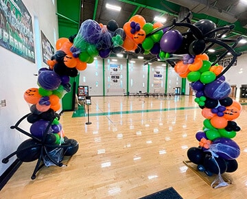 Halloween-themed balloon arch with spiders and web accents for a gym event in Mesa